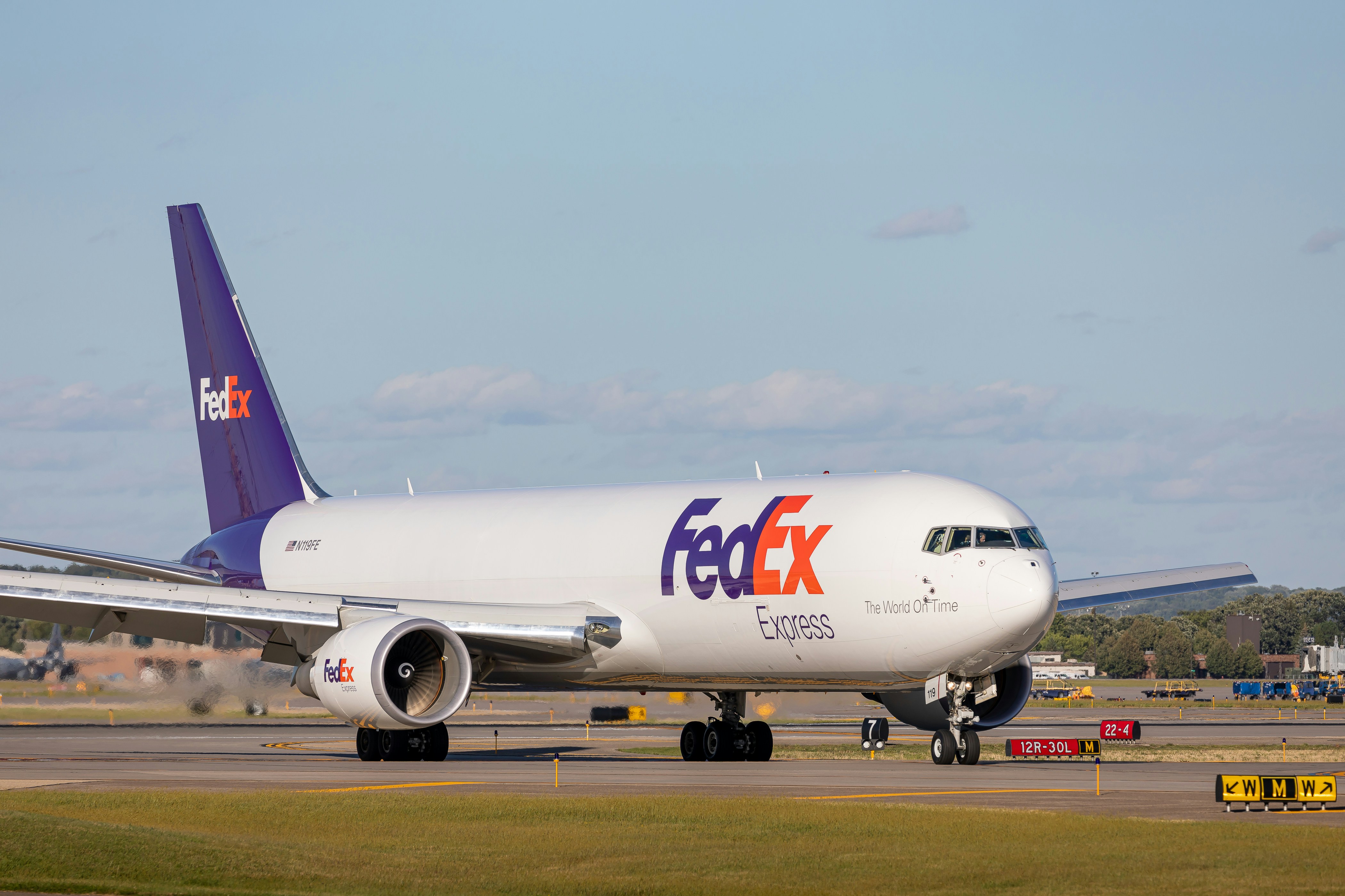 A FedEx Express cargo plane with its logo visible, taxiing on a runway under a partly cloudy sky.