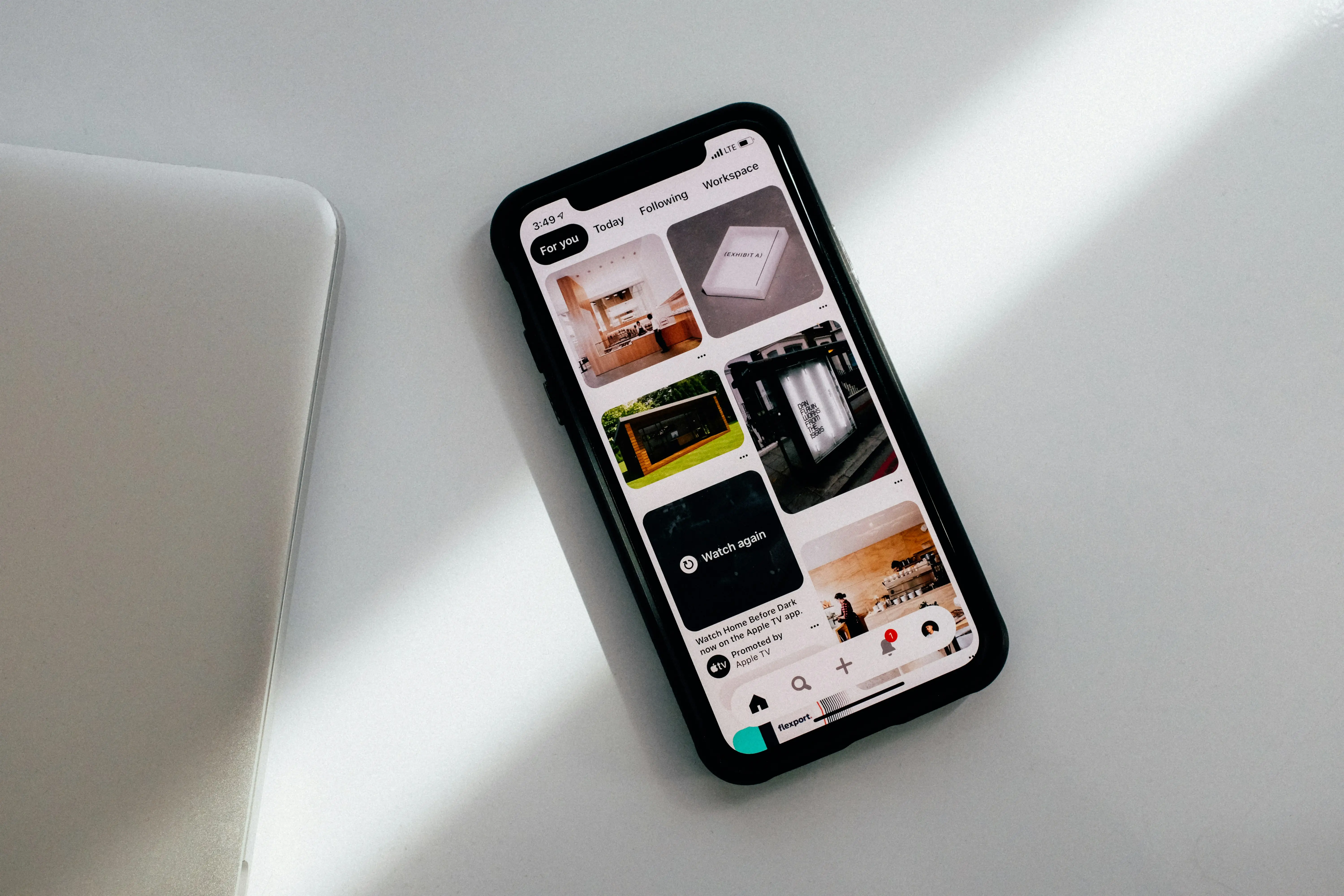 A smartphone displays the Pinterest app beside a laptop on a white surface.