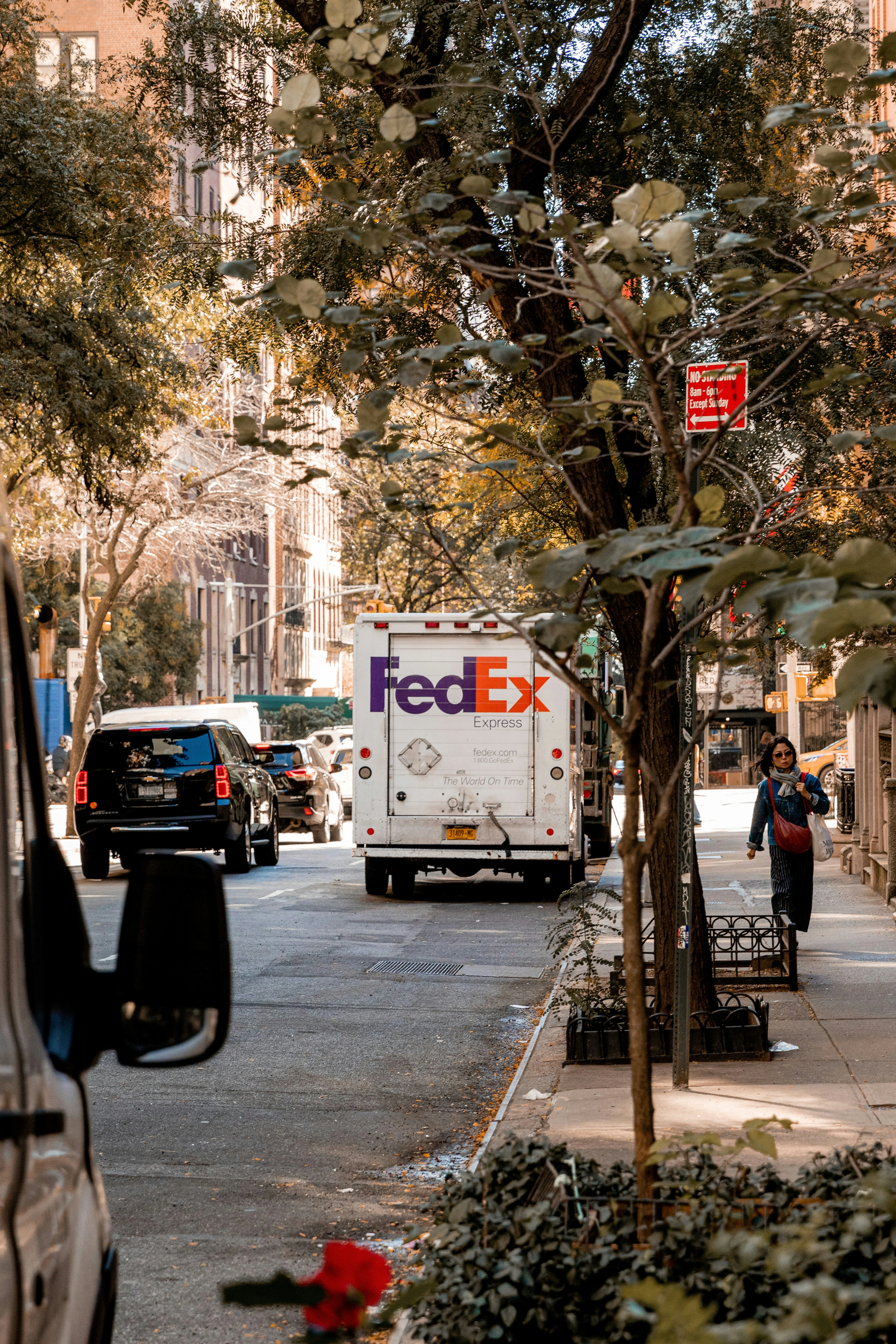 A FedEx truck parked on a city street with trees and buildings in the background.