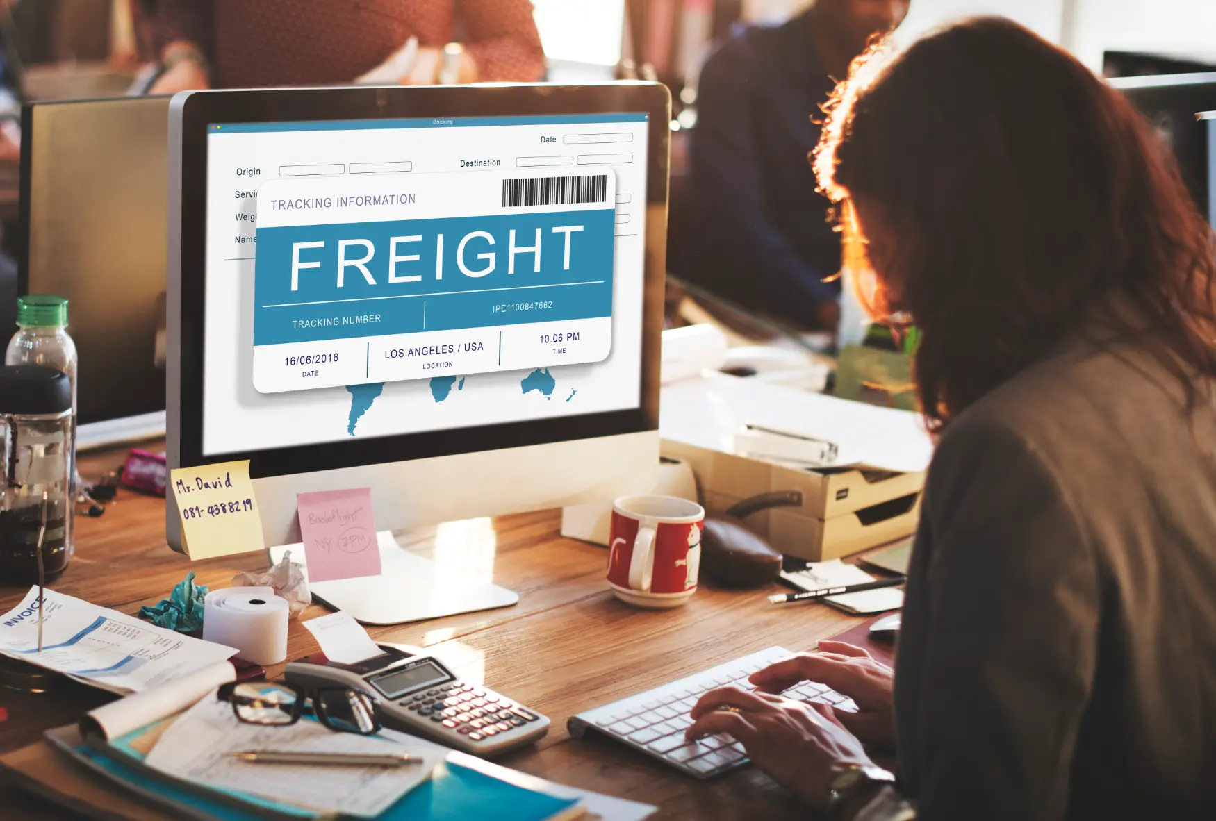 Person working at a desk with a computer screen displaying freight tracking information